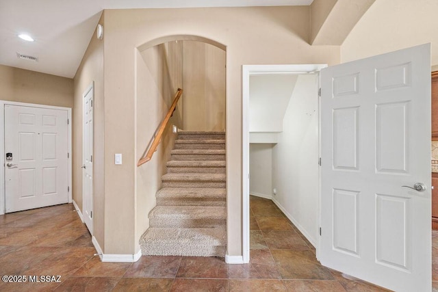 staircase with visible vents, baseboards, and stone finish floor