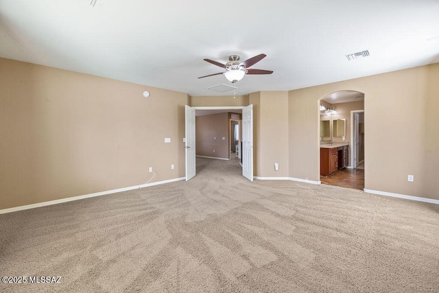 empty room with light colored carpet, visible vents, arched walkways, a ceiling fan, and baseboards