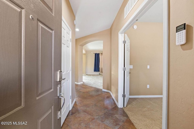 hall featuring visible vents, stone finish flooring, dark carpet, arched walkways, and baseboards