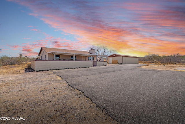 ranch-style home featuring a detached garage, an outbuilding, a chimney, and driveway