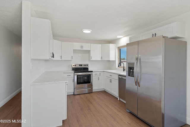 kitchen featuring a sink, stainless steel appliances, light wood-style flooring, and white cabinetry