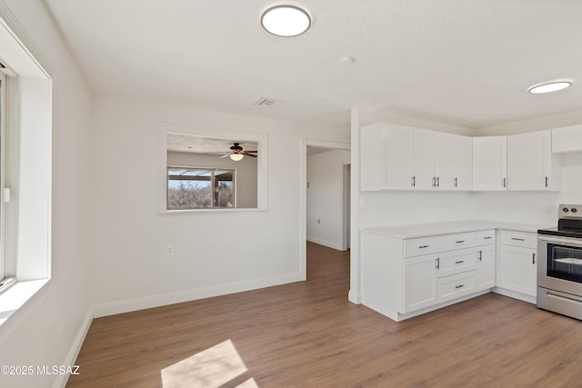 kitchen featuring stainless steel electric range, wood finished floors, light countertops, and white cabinetry