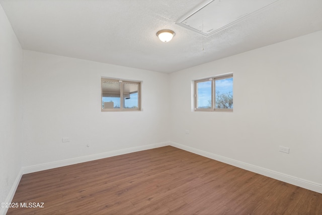 spare room with a textured ceiling, attic access, baseboards, and wood finished floors