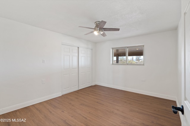 unfurnished bedroom with a closet, a textured ceiling, baseboards, and wood finished floors