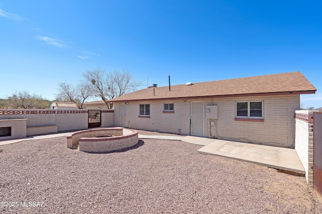 rear view of property with brick siding, a fire pit, fence, and a gate