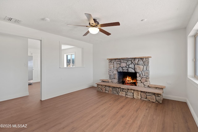 living room with visible vents, baseboards, a fireplace, wood finished floors, and a textured ceiling