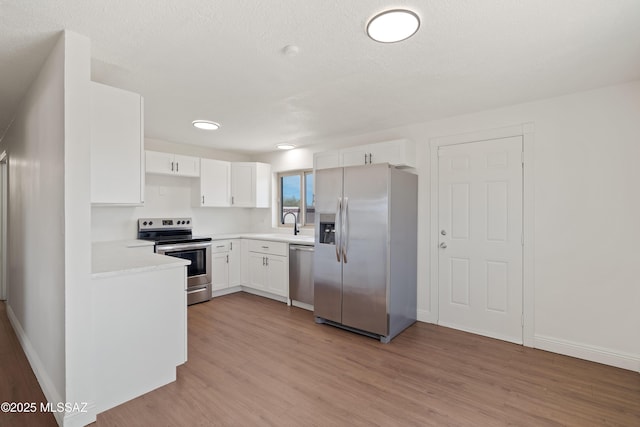 kitchen with light wood-style flooring, appliances with stainless steel finishes, white cabinets, light countertops, and baseboards