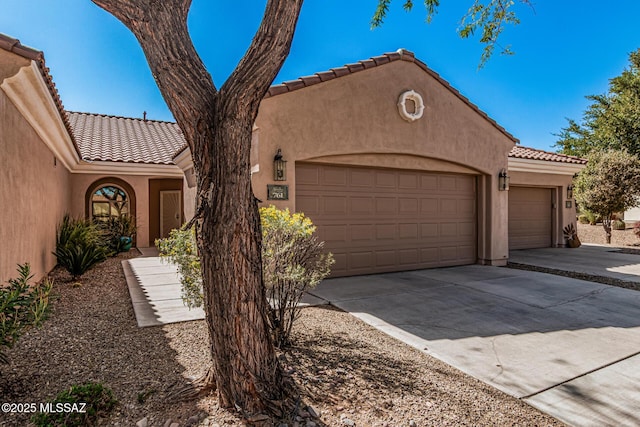 mediterranean / spanish house with stucco siding, a garage, concrete driveway, and a tiled roof