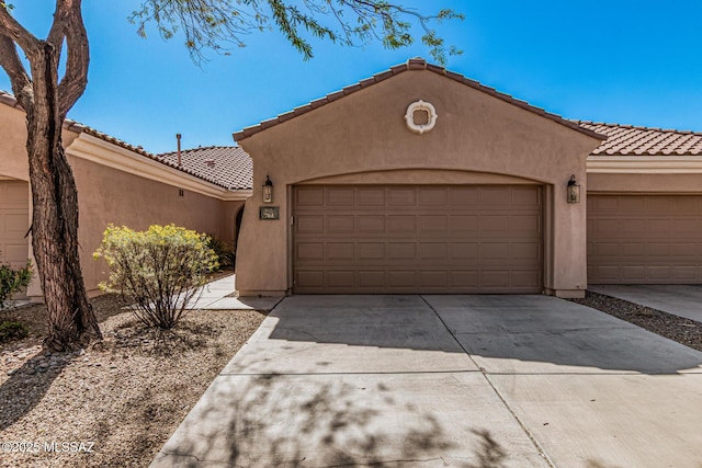 mediterranean / spanish house with a tiled roof, stucco siding, an attached garage, and concrete driveway