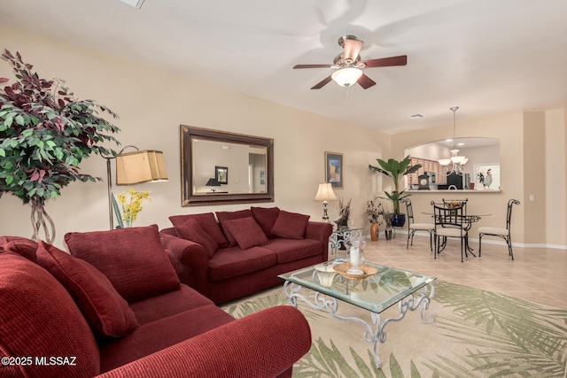 living area featuring tile patterned flooring, ceiling fan with notable chandelier, and baseboards