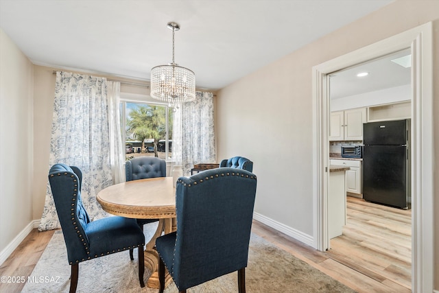 dining space with light wood-style flooring, a notable chandelier, and baseboards