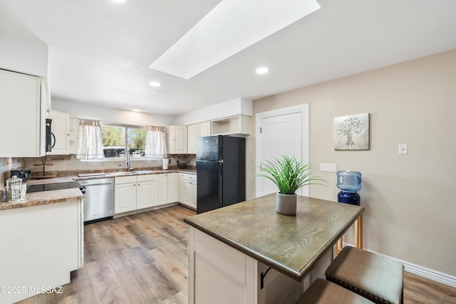 kitchen with light wood-type flooring, tasteful backsplash, stainless steel dishwasher, freestanding refrigerator, and a skylight