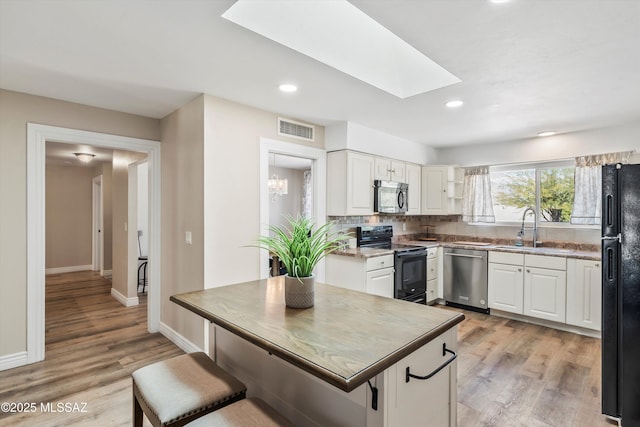 kitchen with visible vents, black appliances, a sink, a skylight, and white cabinets