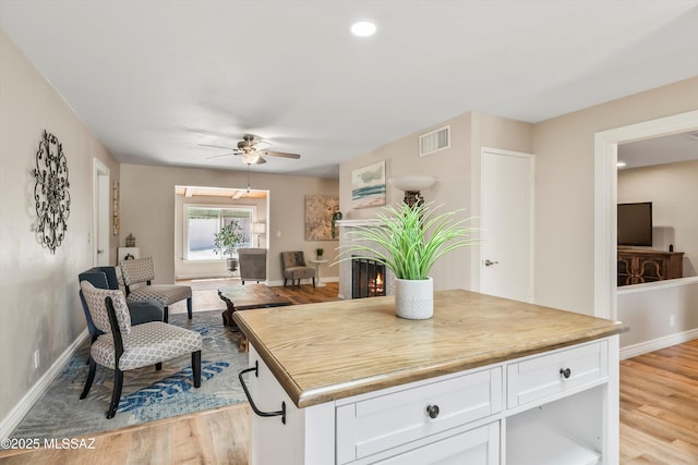 kitchen with visible vents, white cabinetry, light wood-style floors, a lit fireplace, and baseboards