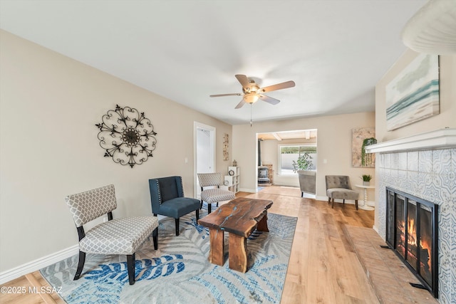 living room with baseboards, ceiling fan, a tiled fireplace, and light wood finished floors