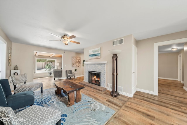 living room featuring visible vents, a ceiling fan, wood finished floors, baseboards, and a brick fireplace