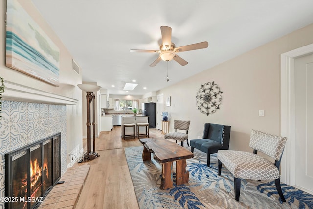 living area with visible vents, a brick fireplace, light wood-style flooring, a skylight, and a ceiling fan