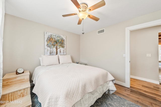 bedroom featuring ceiling fan, visible vents, baseboards, and wood finished floors