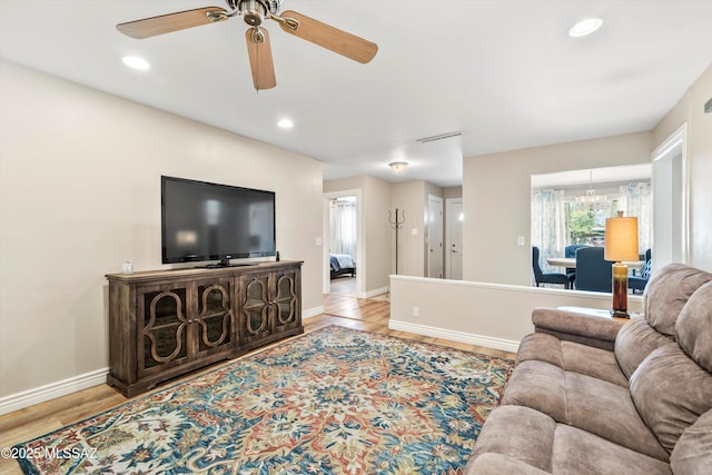 living room with recessed lighting, ceiling fan with notable chandelier, light wood-type flooring, and baseboards