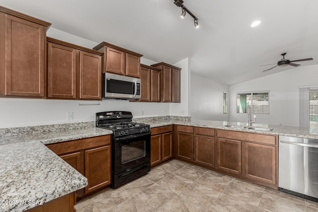 kitchen featuring ceiling fan, vaulted ceiling, light stone counters, appliances with stainless steel finishes, and a sink