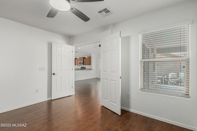 spare room with dark wood-type flooring, baseboards, visible vents, and ceiling fan