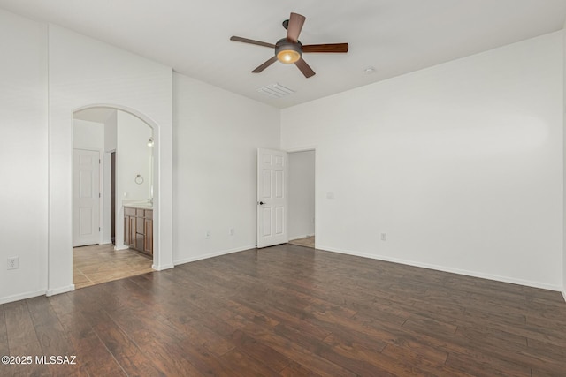 empty room featuring visible vents, baseboards, ceiling fan, dark wood finished floors, and arched walkways