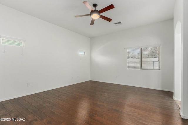 empty room with a ceiling fan, visible vents, dark wood-style flooring, and baseboards