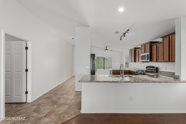 kitchen featuring light stone counters, a peninsula, a sink, vaulted ceiling, and appliances with stainless steel finishes