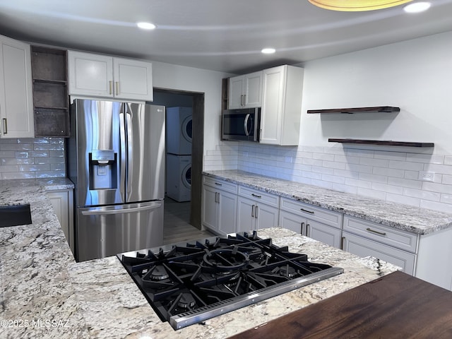 kitchen featuring light stone countertops, open shelves, stainless steel appliances, stacked washer and clothes dryer, and tasteful backsplash