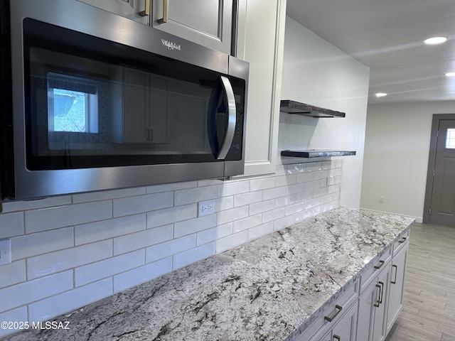 kitchen featuring light stone counters, open shelves, light wood-style flooring, stainless steel microwave, and tasteful backsplash