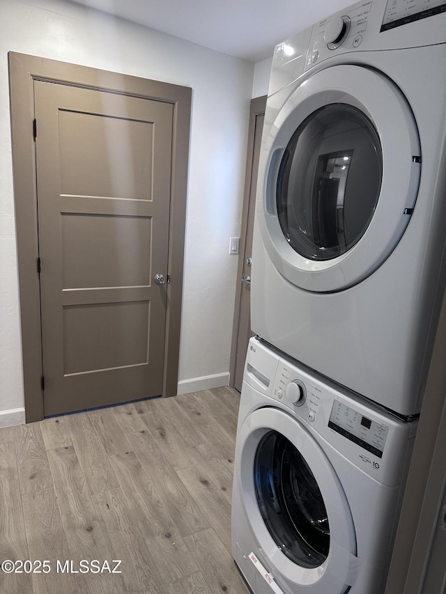 washroom with laundry area, baseboards, light wood finished floors, and stacked washing maching and dryer