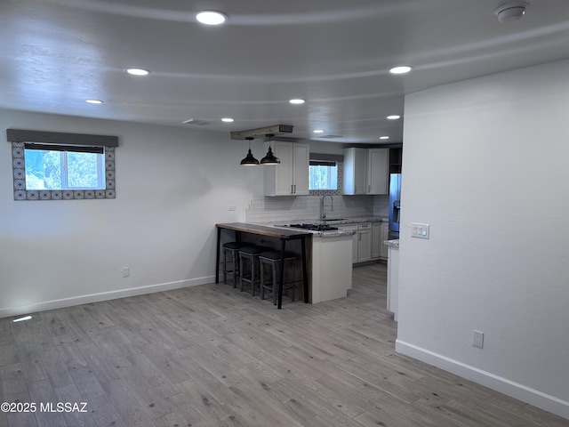 kitchen featuring backsplash, a breakfast bar area, light wood-type flooring, a peninsula, and a sink