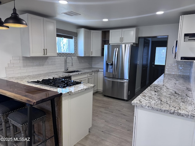 kitchen with visible vents, a sink, gas stovetop, a peninsula, and stainless steel fridge with ice dispenser