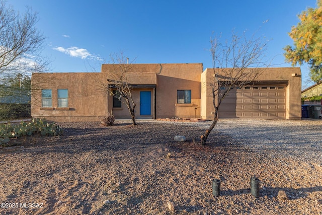 adobe home with an attached garage, driveway, and stucco siding