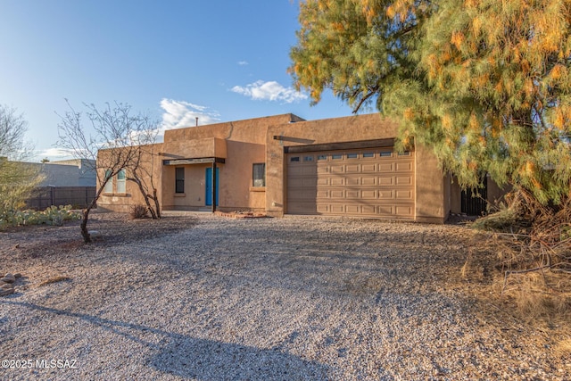 pueblo-style home with gravel driveway, an attached garage, fence, and stucco siding