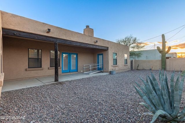 back of property at dusk with a patio area, fence, a chimney, and stucco siding