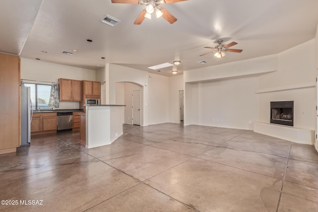 unfurnished living room with visible vents, a fireplace with raised hearth, a ceiling fan, arched walkways, and concrete floors