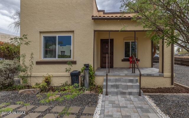 entrance to property with covered porch, a tile roof, and stucco siding