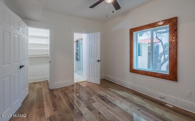 unfurnished bedroom featuring a spacious closet, wood finished floors, baseboards, and ceiling fan