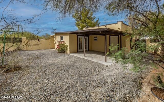 rear view of property featuring fence, french doors, and stucco siding