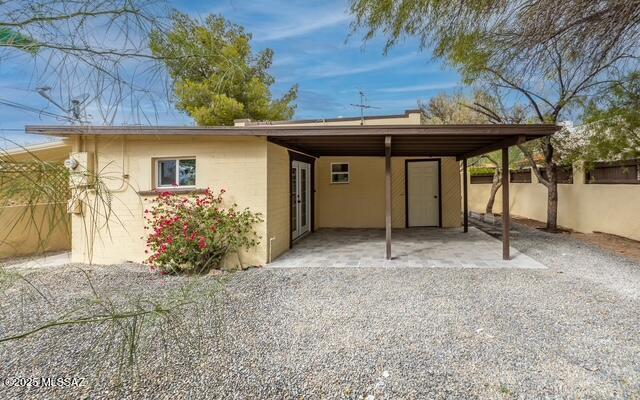 rear view of house with a carport, fence, and stucco siding