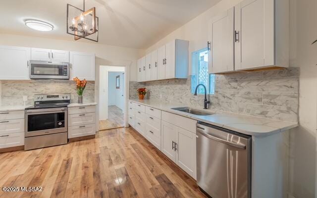 kitchen with light wood-style flooring, a sink, appliances with stainless steel finishes, white cabinets, and light countertops