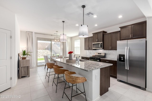 kitchen with visible vents, stainless steel appliances, decorative backsplash, light stone countertops, and dark brown cabinets