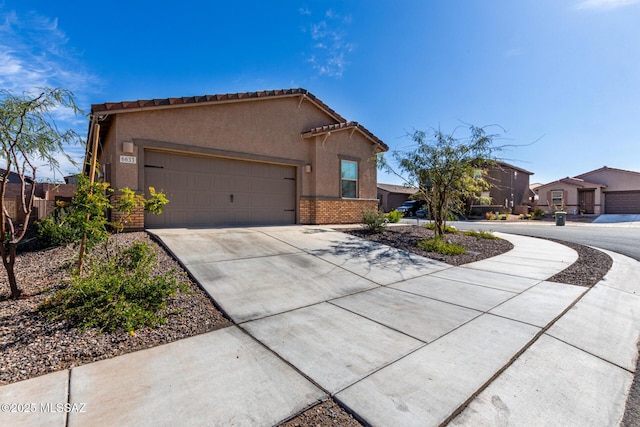 view of front of property with stucco siding, driveway, a tile roof, an attached garage, and brick siding