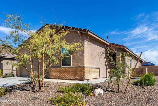 view of side of home with concrete driveway, fence, brick siding, and stucco siding