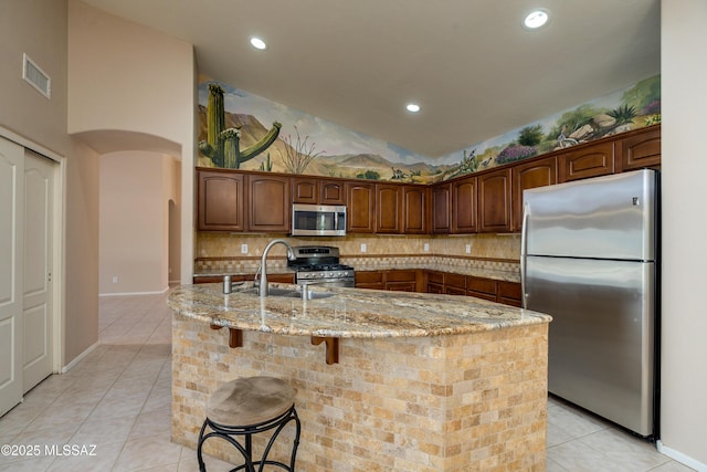 kitchen with light stone counters, stainless steel appliances, arched walkways, light tile patterned floors, and decorative backsplash