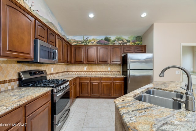 kitchen featuring tasteful backsplash, light stone countertops, light tile patterned flooring, stainless steel appliances, and a sink