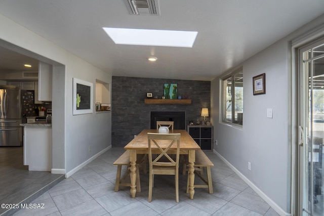 dining area featuring visible vents, a skylight, light tile patterned flooring, baseboards, and a brick fireplace