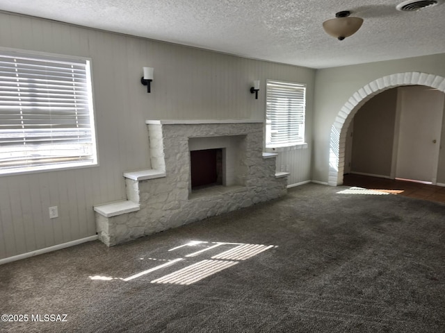 unfurnished living room featuring a fireplace, visible vents, arched walkways, and carpet floors