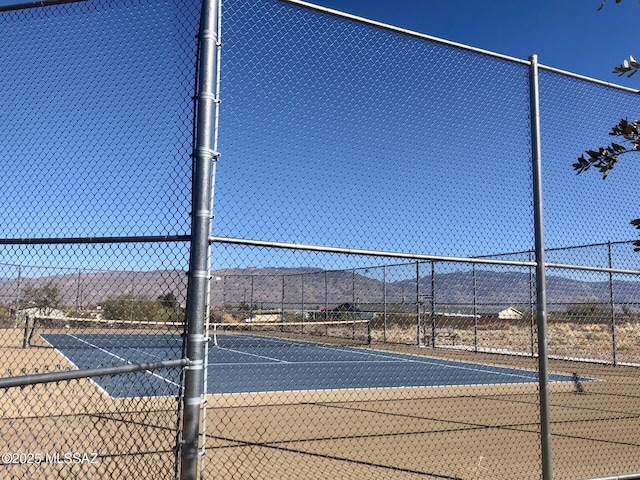 view of tennis court with a mountain view and fence